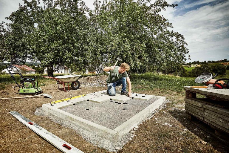 Muž pokladá terasové dosky na pripravený povrch v záhrade