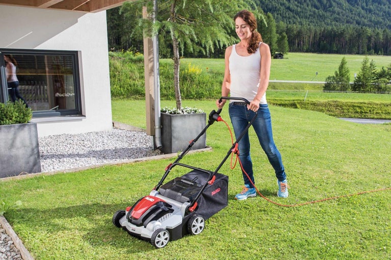 Žena používa elektrickú kosačku na trávu v záhrade.