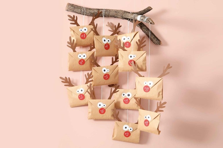 Adventný kalendár s papierovými obálkami, jelením parožím a nálepkami s číslami, zavesený na vetve