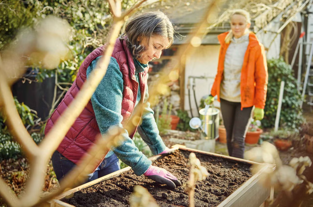 Dve ženy pracujú na záhrade s vyvýšeným záhonom a kanvou na polievanie.