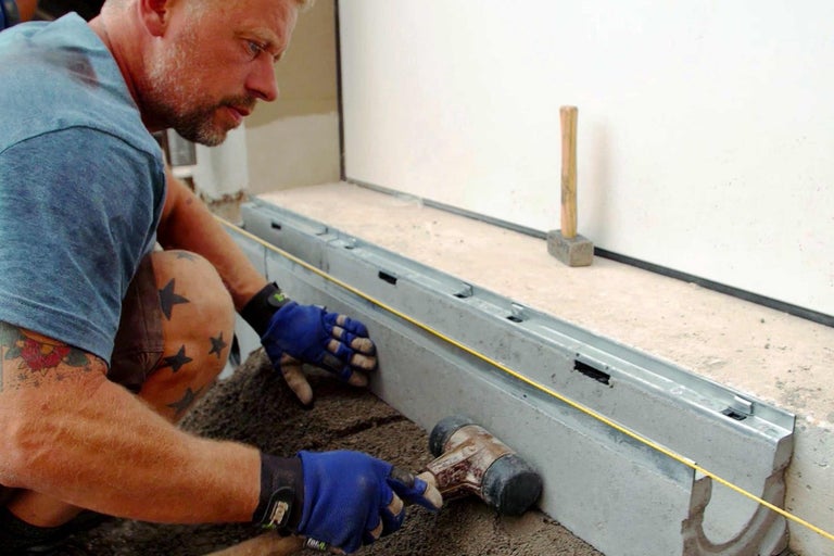 Muž opracováva betónový obrubník kladivom.