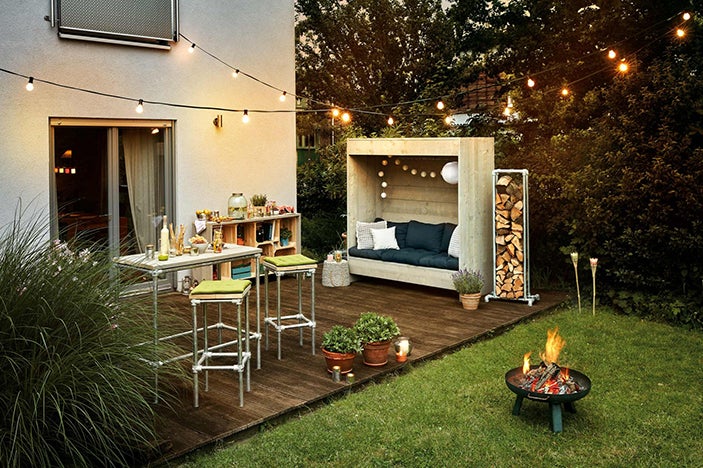 Vonkajší priestor so sedacou súpravou, skladom dreva, ohniskom a svetelnou reťazou pre útulnú atmosféru.