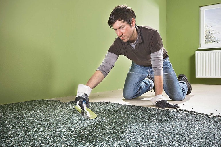 Muž pokladá kamenný koberec hladidlom v interiéri.