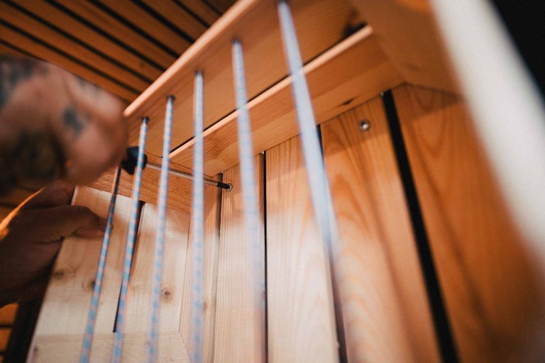 Osoba montuje drevenú policu pomocou skrutiek a skrutkovača.