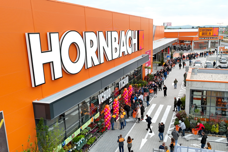 Hornbach Logo na oranžovej fasáde hobbymarketu s dlhým radom zákazníkov pred vchodom.