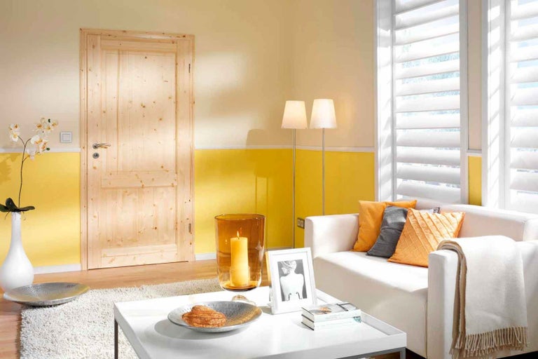 Obývacia izba s drevenými dverami, bielym gaučom, žalúziami a dekoratívnymi prvkami.