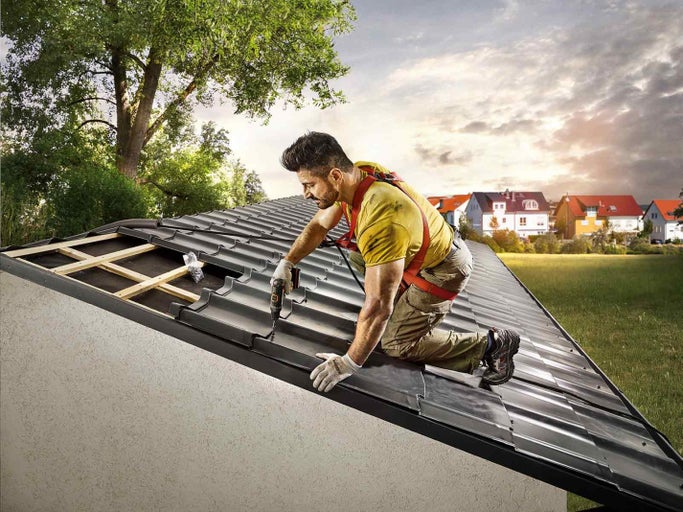 Muž upevňuje strešné tašky akumulátorovým skrutkovačom