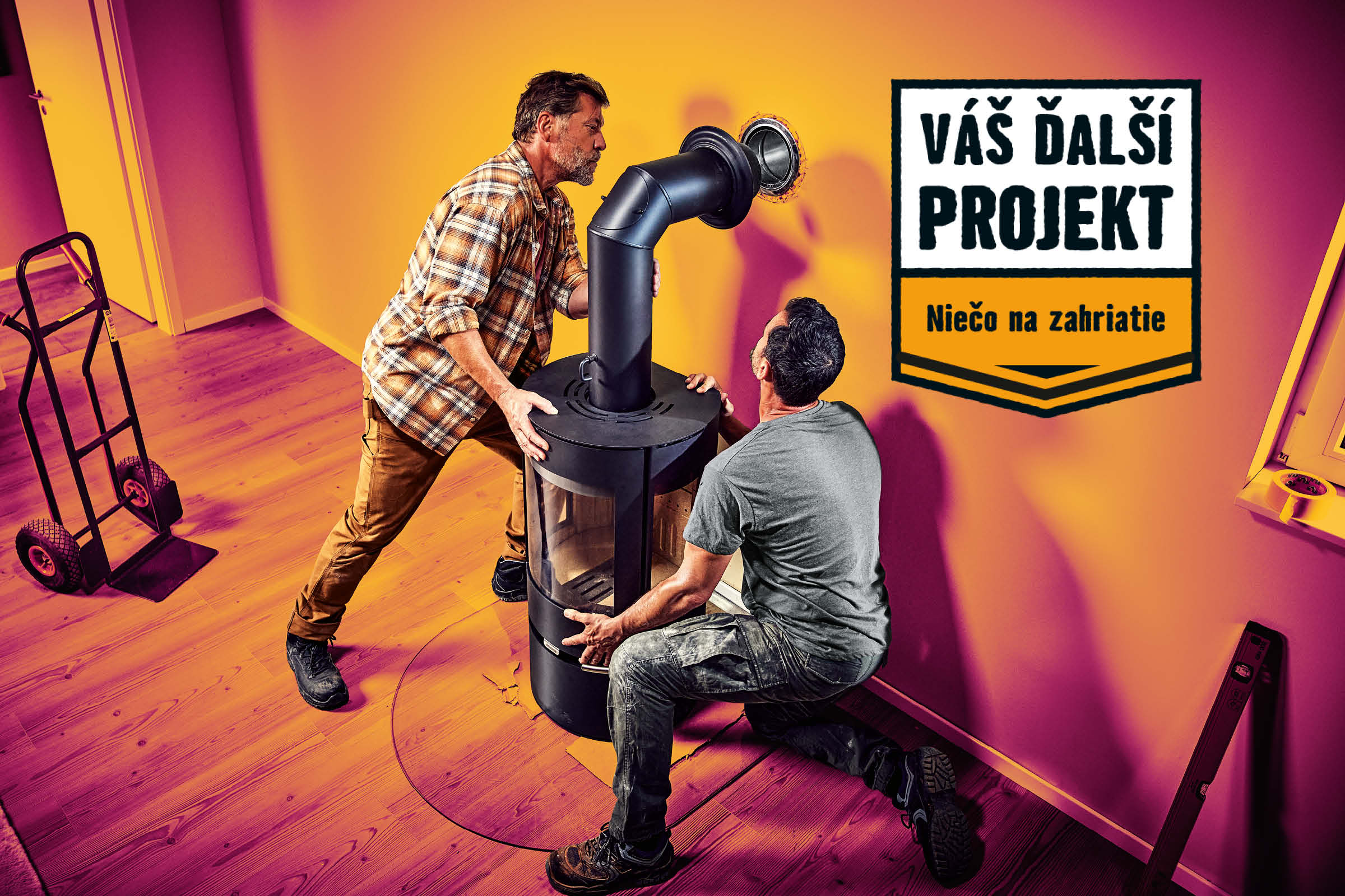 Dvaja remeselníci inštalujú v miestnosti kachle na drevo. V miestnosti sa nachádza ručný vozík a vodováha. Nápis: Váš ďalší projekt. Niečo na zahriatie.