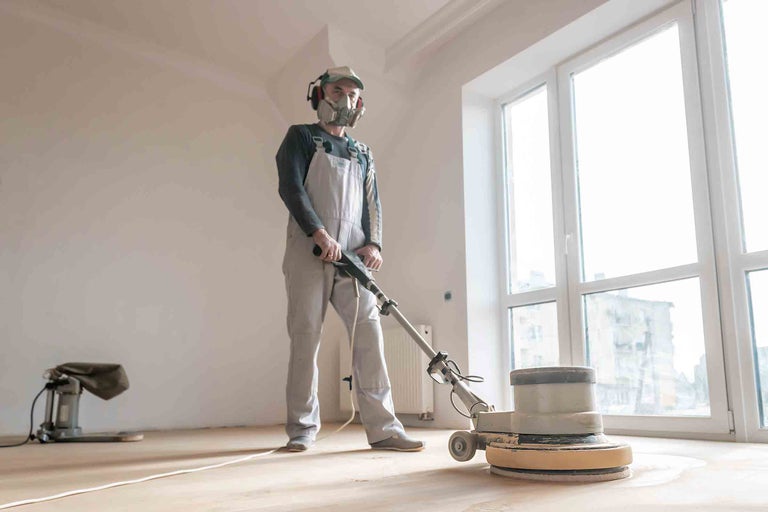Remeselník brúsi drevenú podlahu podlahovou brúskou