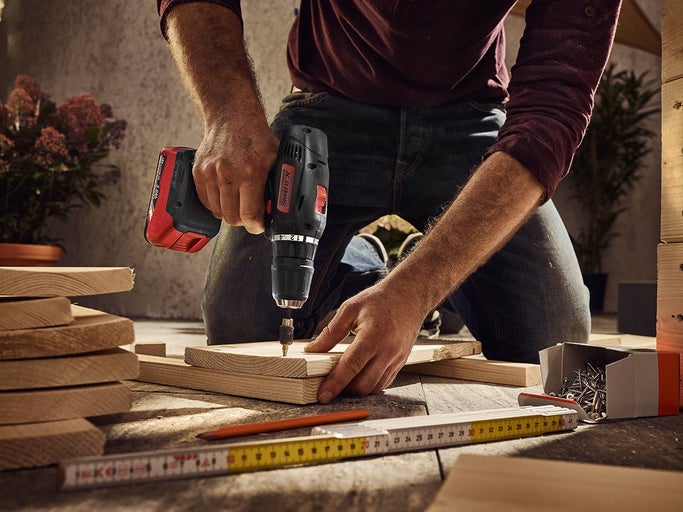 Muž pracuje s akumulátorovým vŕtacím skrutkovačom na drevenom projekte, nástroje sú pripravené