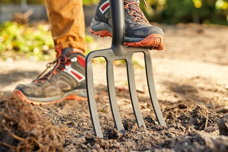 Detailný záber záhradných vidiel zapichnutých do zeme, zatiaľ čo na nich stojí osoba nohou.