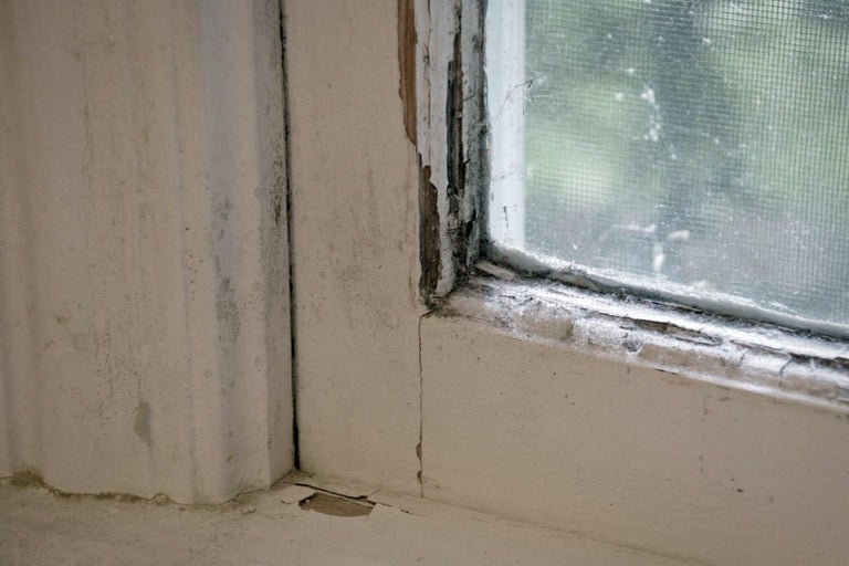 Detail rámu okna s odlupujúcou sa farbou a známkami poškodenia vlhkosťou.