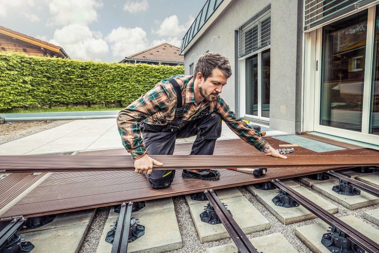 Muž pokladá terasové dosky vonku.