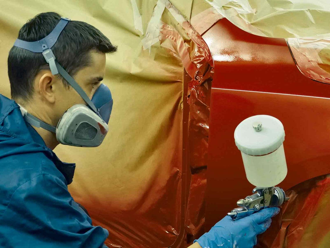 Lakovač nanáša farbu na auto striekacou pištoľou