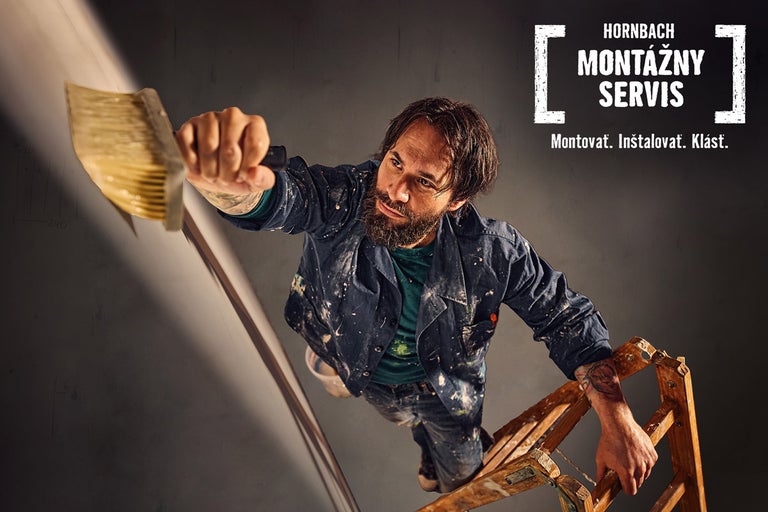 Remeselník stojí na rebríku a maľuje stenu. Montážny servis Hornbach.