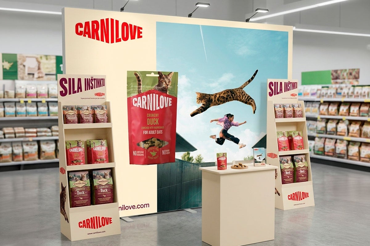 Predajný stánok Carnilove s krmivom pre mačky, produktovými stojanmi a veľkým reklamným bannerom vo svetlom obchode.