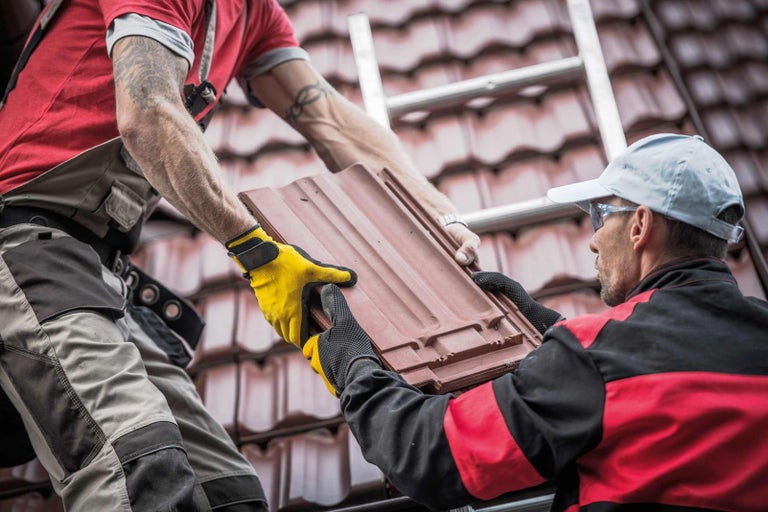 Dvaja pokrývači pokladajú škridly na strechu.