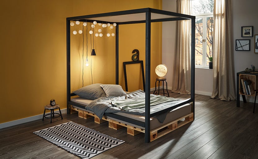 Spálňa s nebeskou posteľou z drevených paliet, zdobená svetelnými reťazami