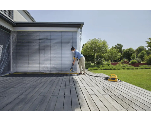 Žena strieka drevenú terasu pomocou striekacieho systému