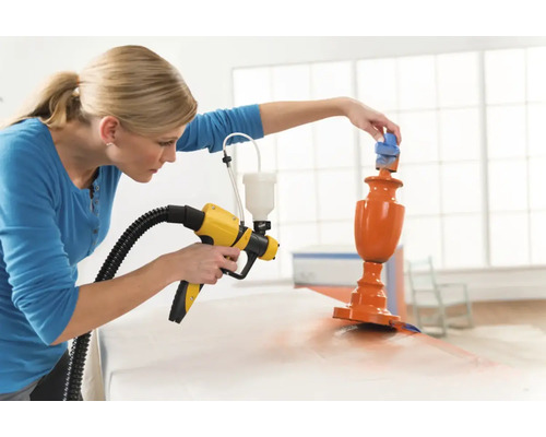 Žena používa striekaciu pištoľ na lakovanie objektu.