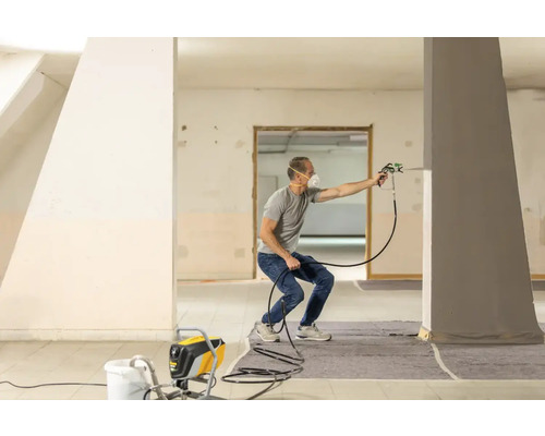 Muž používa striekacie zariadenie v miestnosti na natieranie stĺpu