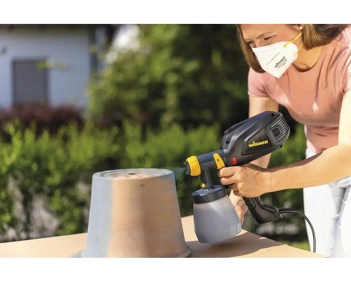 Žena strieka hrniec vonku pomocou striekacieho systému