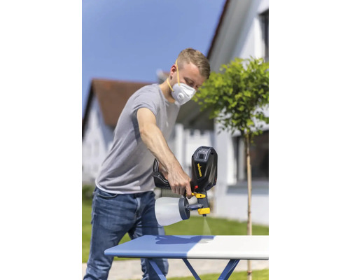 Muž používa striekaciu pištoľ na natieranie stola vonku.