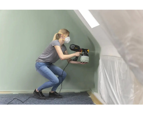 Žena používa striekaciu pištoľ v miestnosti zakrytej fóliou.