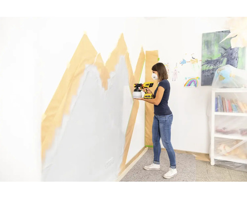 Žena strieka farbu na stenu pomocou striekacieho systému na stenu, ktorá je zakrytá maskovacou páskou.