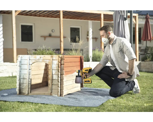 Muž natiera búdu pre psa v záhrade striekacou pištoľou.