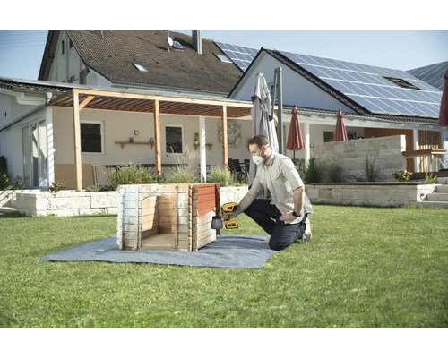Muž natiera psiu búdu striekacou pištoľou v záhrade.