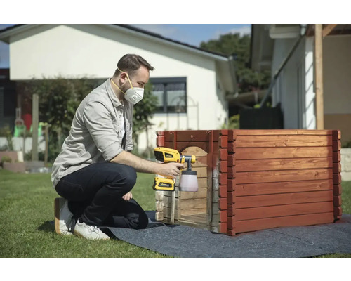 Muž strieka drevo striekacou pištoľou na farby v záhrade.
