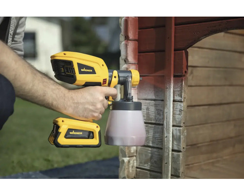 Muž používa striekaciu pištoľ Wagner na natieranie dreveného domu.