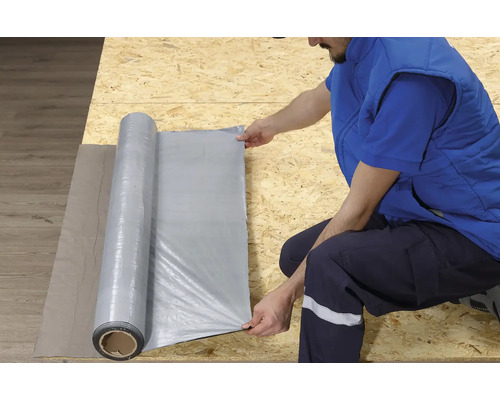 Osoba rozbaľuje stavebnú fóliu na drevenom povrchu.