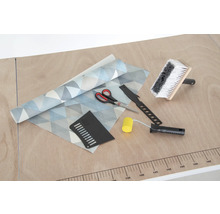 Tapeta s geometrickým vzorom, štetka na lepidlo, prítlačný valček, tapetovací nôž, prítlačná špachtľa a nožnice na stole.