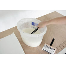 Lepidlo na tapety sa mieša vo vedre s miešadlom, vedľa leží štetka na tapety a tapeta.