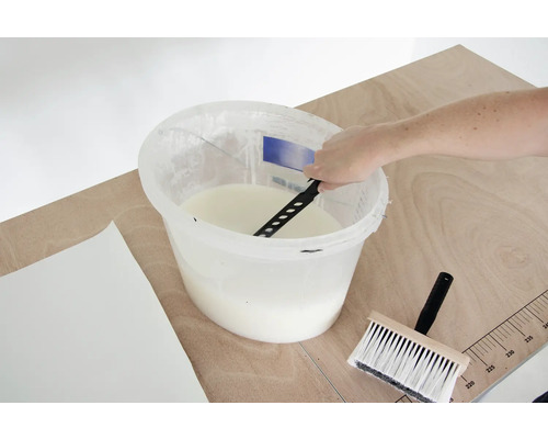 Lepidlo na tapety sa mieša vo vedre s miešadlom, vedľa leží štetka na tapety a tapeta.