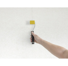 Ruka maľuje stenu valčekom na farbu žlto