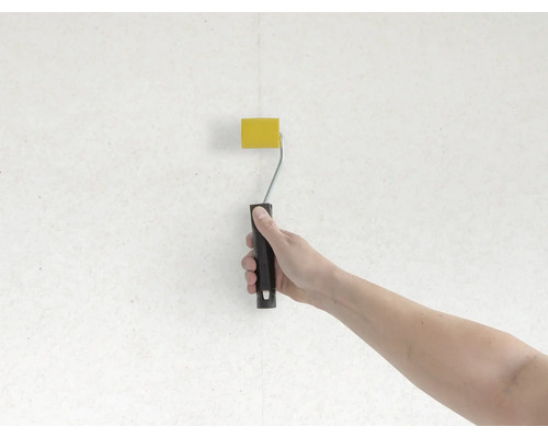 Ruka maľuje stenu valčekom na farbu žlto