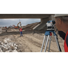 Stavební robotníci vykonávajú geodetické práce s nivelačným prístrojom a meracou latou na stavenisku