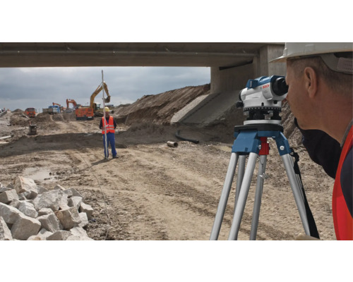 Stavební robotníci vykonávajú geodetické práce s nivelačným prístrojom a meracou latou na stavenisku