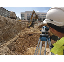 Stavebný robotník používa nivelačný prístroj na stavenisku s bagrom v pozadí