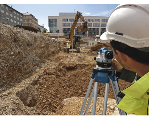 Stavebný robotník používa nivelačný prístroj na stavenisku s bagrom v pozadí