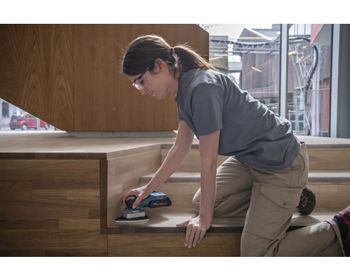 Žena brúsi drevené schodisko brúskou