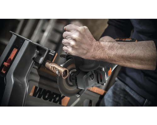 Osoba reže medenú rúrku rozbrusovacou pílou upevnenou v pracovnom stole. Logo WORX.