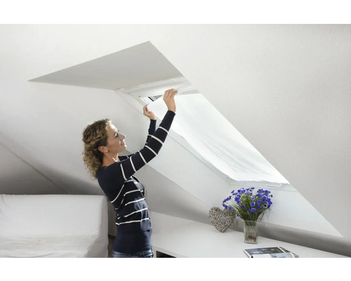 Žena montuje slnečnú roletu na strešné okno vo svetlej podkrovnej izbe.