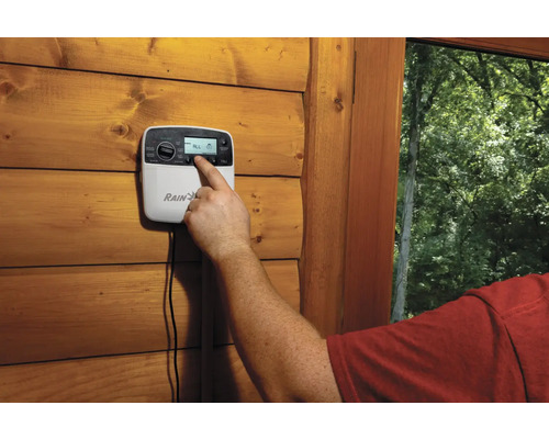 Osoba ovláda zavlažovací počítač na drevenej stene.