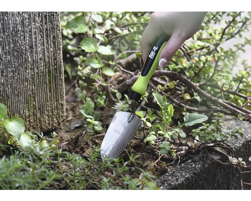 Detailný záber ruky držiacej malú záhradnú lopatku v hline vedľa rastlín