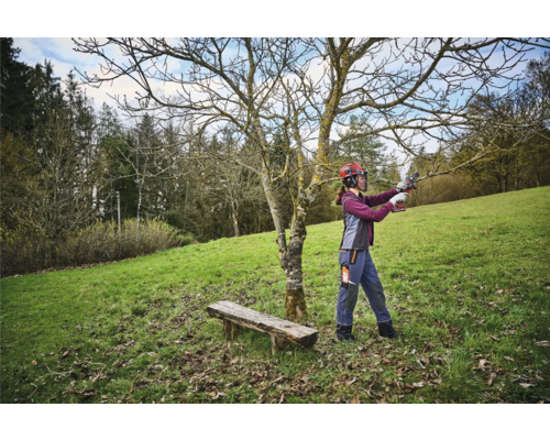 Žena s ochrannou prilbou strihá strom nožnicami na konáre v záhrade.