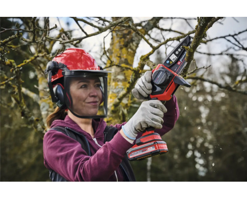 Žena s ochrannou helmou a akumulátorovou reťazovou pílou prerezáva strom
